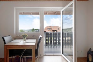 A room with a wooden table, chairs, a vase with flowers, and a balcony with a metal railing.