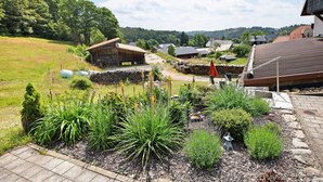 Landelijk landschap met een stenen huis, een houten schuur en een tuin met diverse planten.