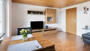 Een moderne woonkamer met een houten plafond, een flatscreen televisie, een eettafel met een bloevas en een ingebouwde houten kast.