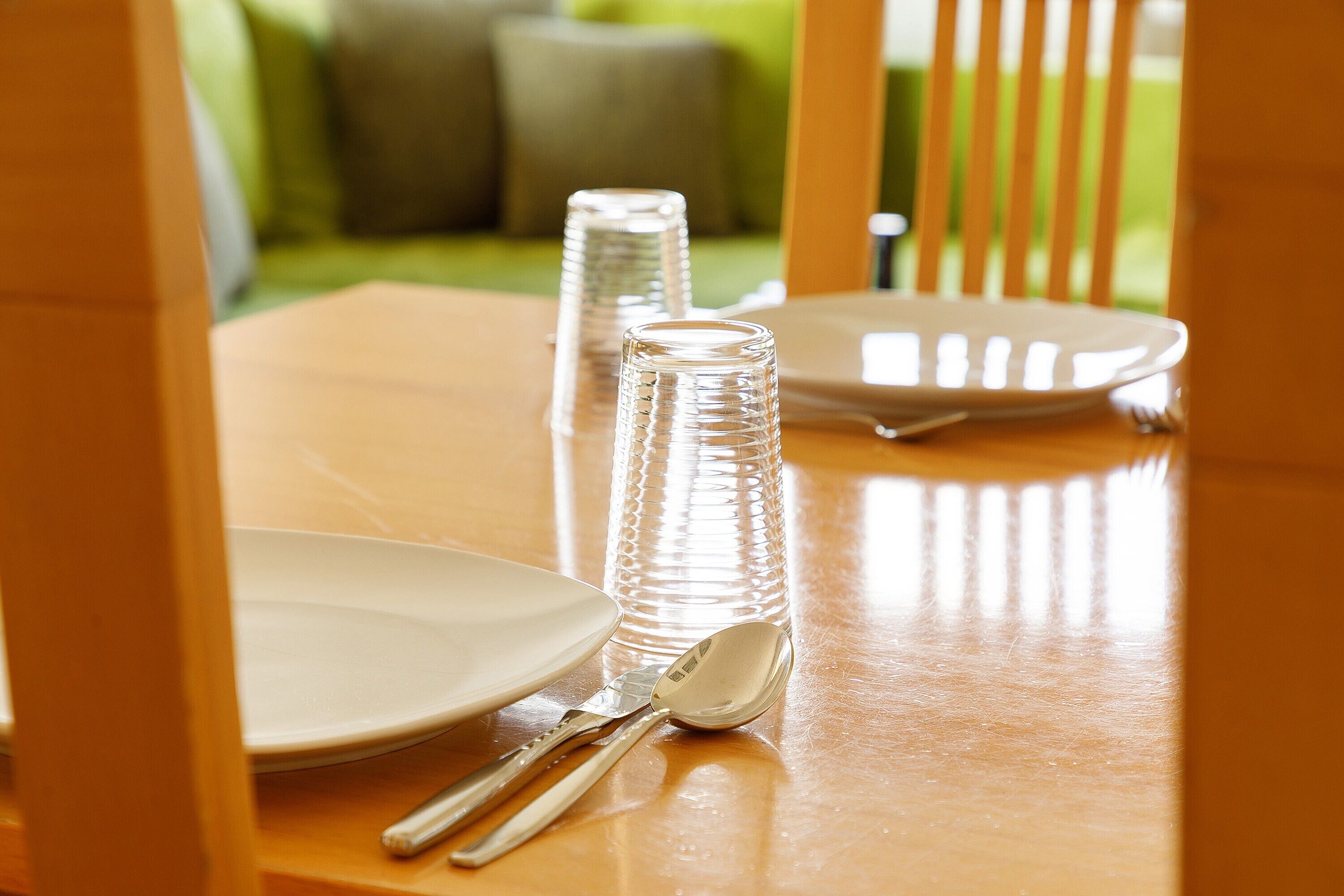 A dining table with a plate, a spoon, and a glass.