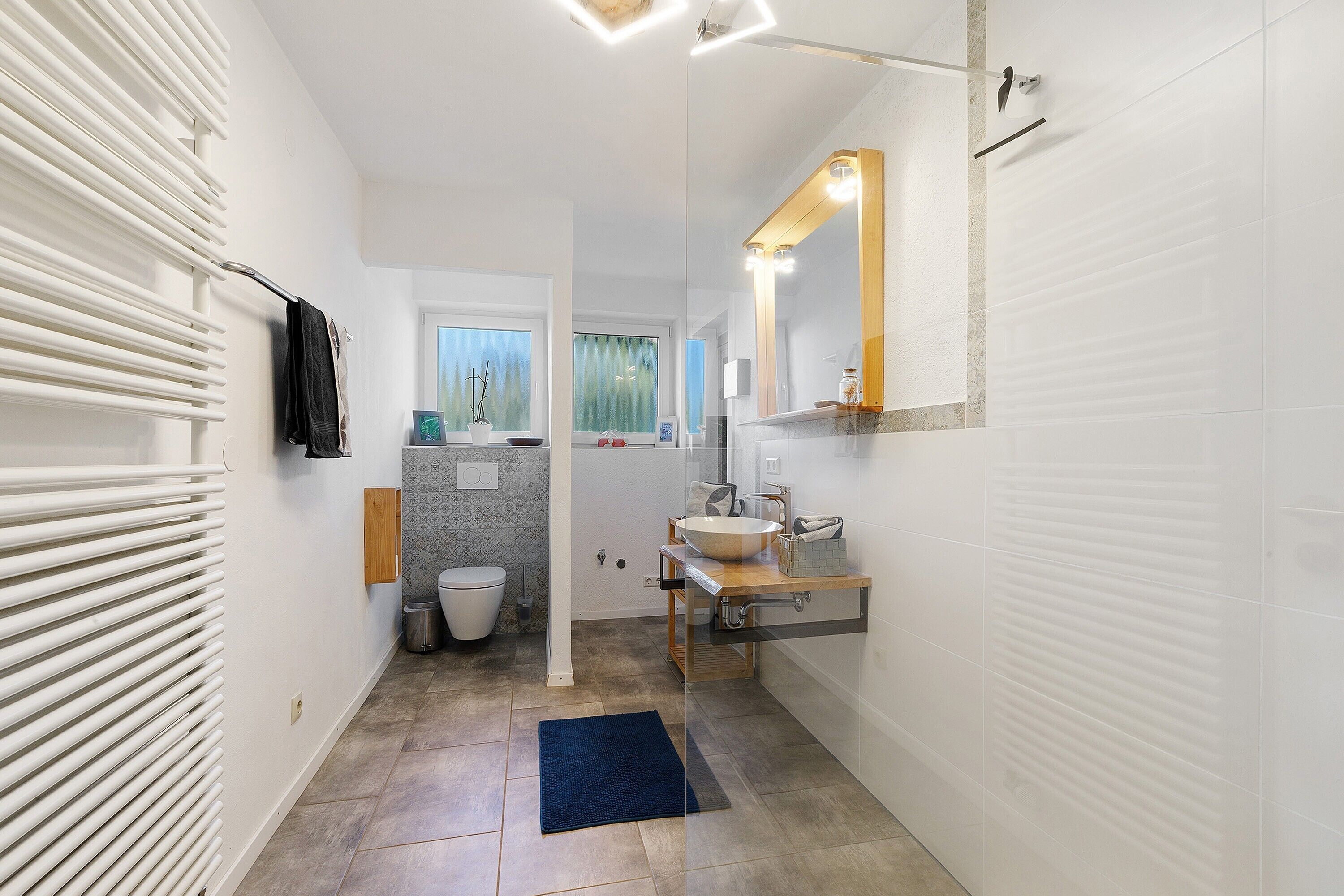 Un baño moderno con un lavamanos, espejo y toallero blancos.