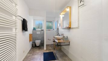 Un baño moderno con un lavamanos, espejo y toallero blancos.
