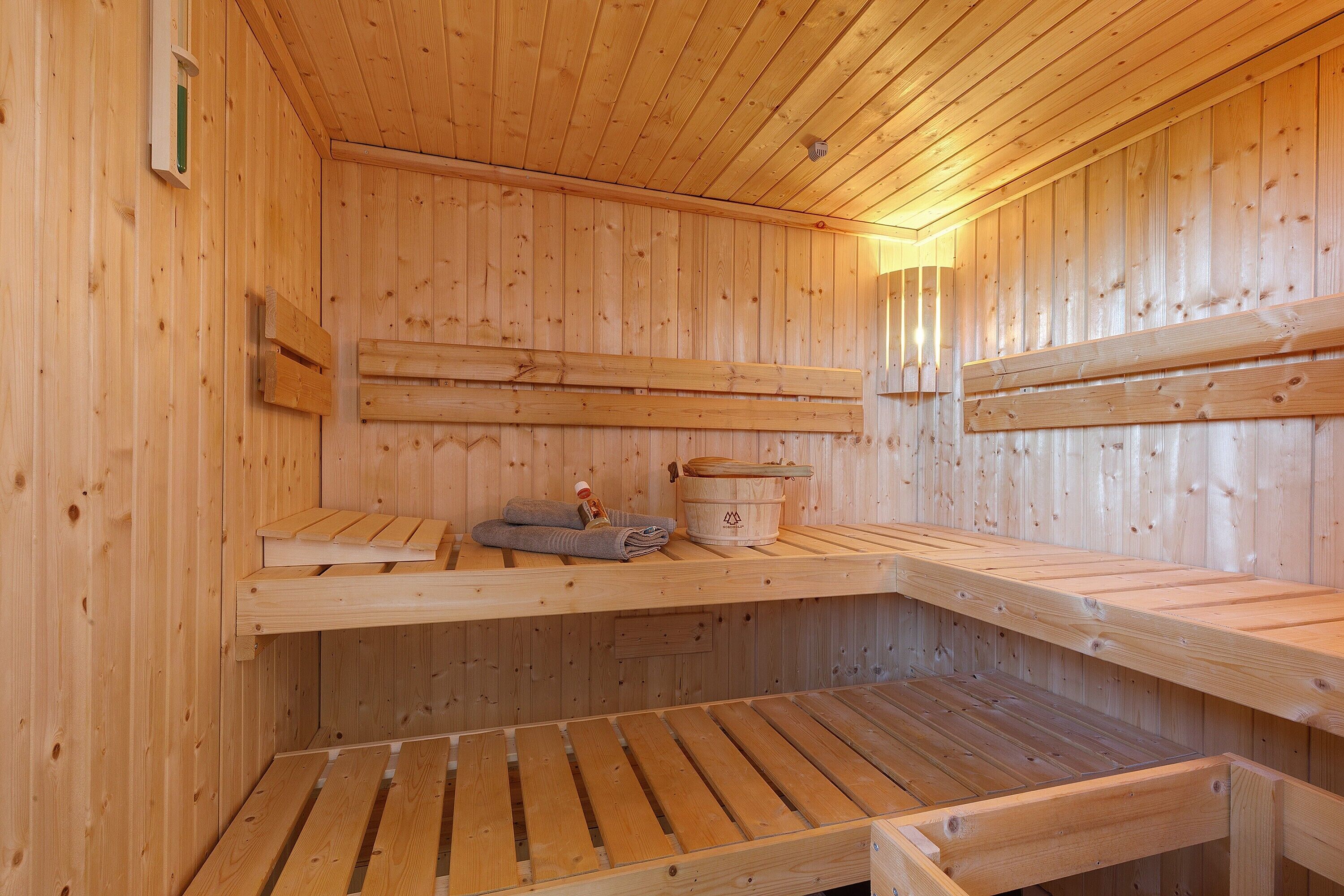 A sauna with wooden benches, a towel, and a wooden bucket.