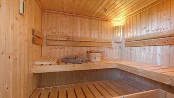 A sauna with wooden benches, a towel, and a wooden bucket.