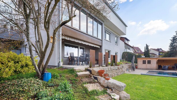 Una casa moderna de dos pisos con un patio, una piscina y un jardín bien cuidado.