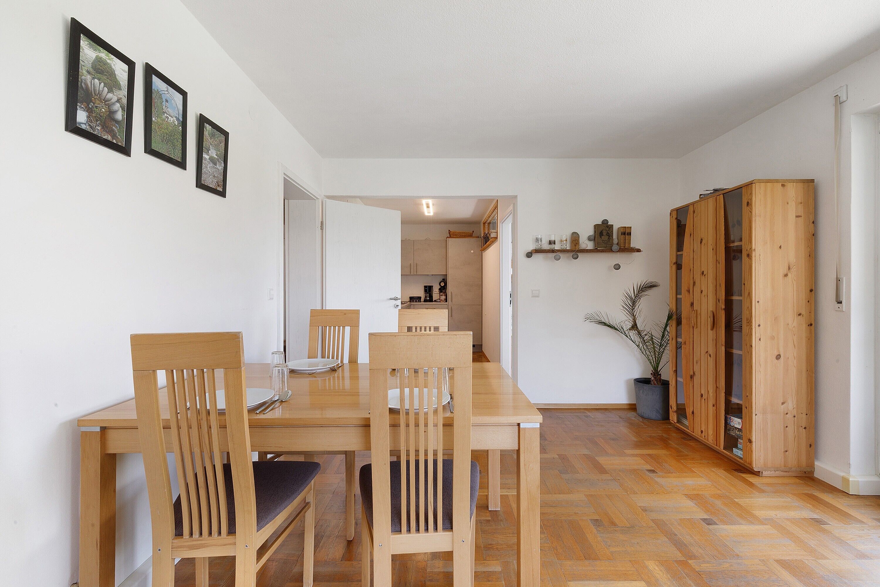 A dining area with wooden chairs and a table, a hallway leading to a kitchen, and a wooden wardrobe.