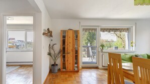 Un interior con un armario de madera, una planta en maceta, una mesa de comedor con sillas y vistas a través de una ventana.