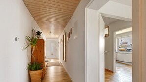 Un pasillo con suelo de madera, paredes blancas y vistas a un paisaje urbano a través de una puerta abierta.