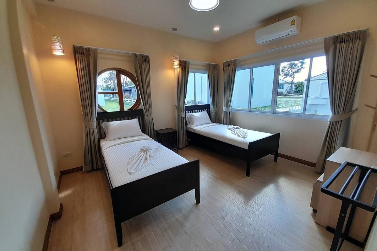 A hotel room with two single beds, a small table, and a window with curtains.