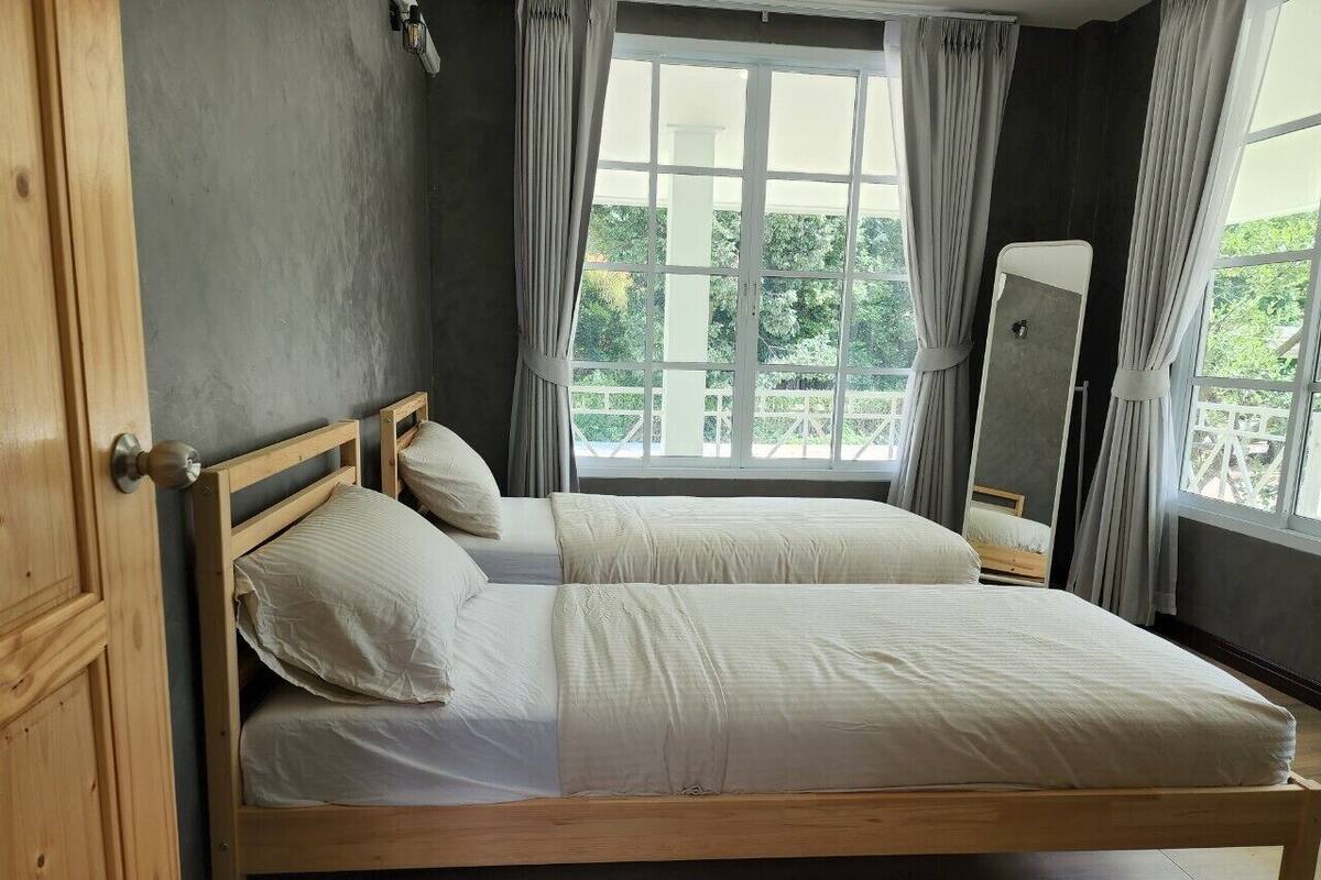 A single bed with a wooden frame and white bedding in a room with a large window and curtains.