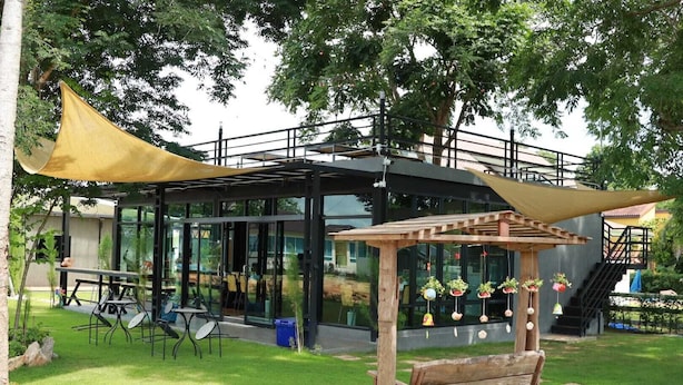 A modern outdoor area with a glass-enclosed structure, a wooden pergola, and a table with chairs. - Thungtheiyngvalley Khaoyai (Pak Chong)