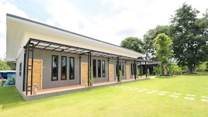 A modern house with a covered patio, a well-maintained lawn, and a large tree in the background. - Thungtheiyngvalley Khaoyai (Pak Chong)