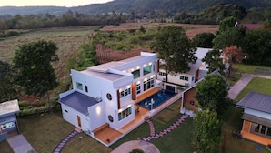 A modern two-story house with a large swimming pool, surrounded by a well-maintained lawn and trees. - Thungtheiyngvalley Khaoyai (Pak Chong)