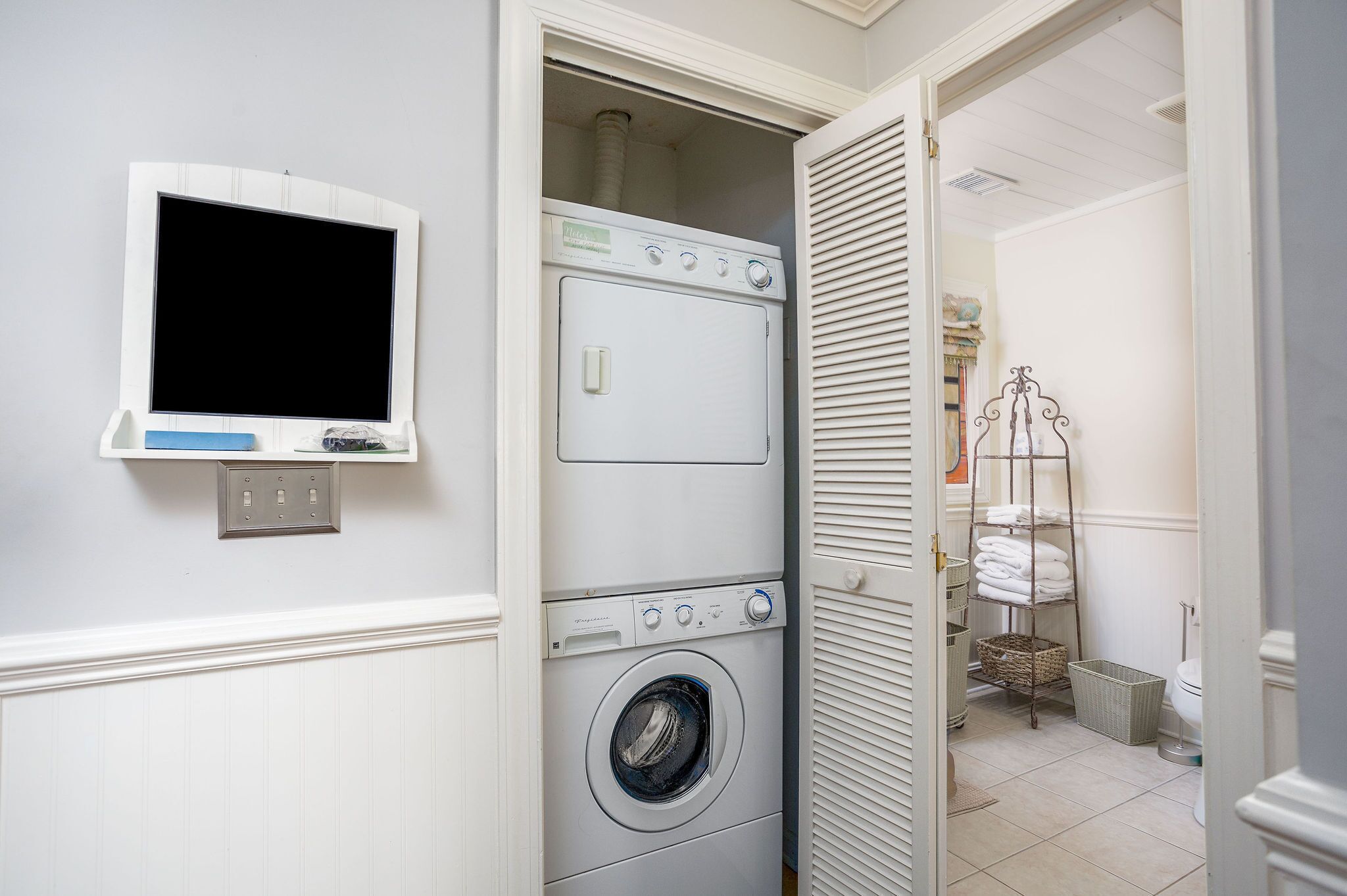 Une buanderie équipée d’un lave-linge et d’un sèche-linge superposés, d’un téléviseur fixé au mur et d’un porte-serviettes.