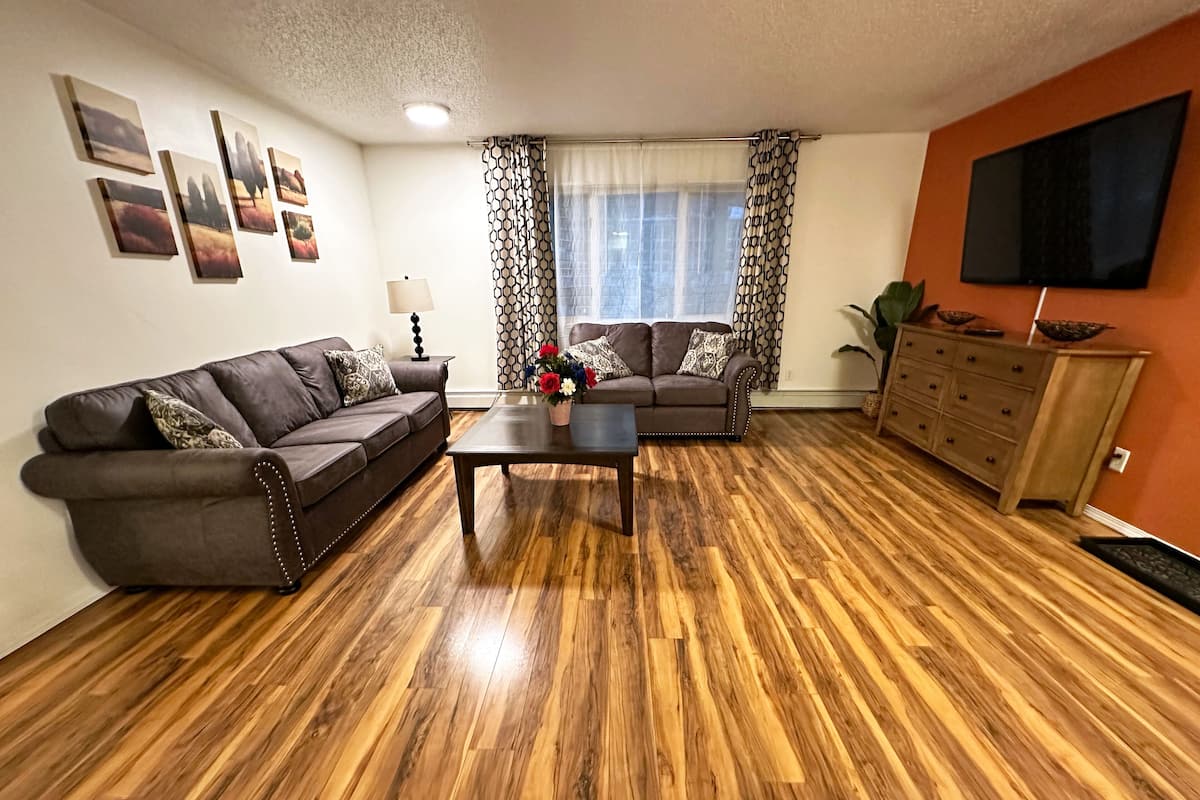 A living room with a wooden floor, two sofas, a coffee table, a TV, and a cabinet.