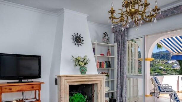 Una sala de estar con chimenea, televisor, estantería y vistas a un balcón con mobiliario exterior.