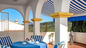 Una terraza con una mesa redonda, sillas a rayas azules y una estatua.
