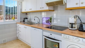 Una cocina moderna con armarios blancos, encimera de madera, lavavajillas integrado, horno y cafetera.