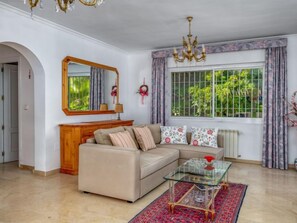 A living room with a beige sofa, a glass coffee table, and a large window with curtains. - El Chaparral by Interhome (Coin)