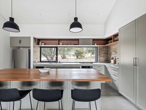 A modern kitchen with a wooden island, black chairs, and pendant lights.
