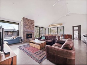 A spacious living room with a stone fireplace, leather sofas, a coffee table, and large windows.