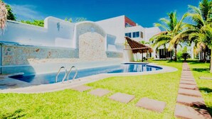 Una piscina con una pared de piedra, una estructura de techo de paja y palmeras.