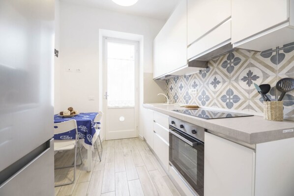 A compact kitchen with white cabinets, a patterned backsplash, a stove, and a dining area with a table and chairs.
