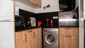 A compact kitchen with a microwave, toaster, kettle, coffee maker, and a washing machine.