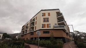 A multi-story residential building with balconies, a pedestrian pathway, and surrounding vegetation.