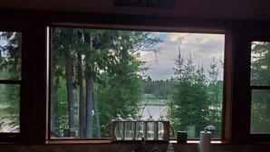 Une cuisine avec une fenêtre donnant sur un lac et des arbres, un évier et une cuisinière.