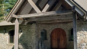 Une maison en pierre avec un porche en bois, une grande porte en bois et une cheminée en pierre.