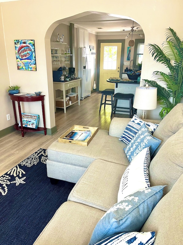 A living room with a sofa, coffee table, and a dining area with a kitchen in the background.