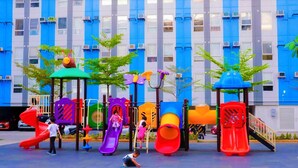 Ein Spielplatz mit mehreren Rutschen und Klettergerüsten vor einem Gebäude mit blauen und grauen Außenwänden.