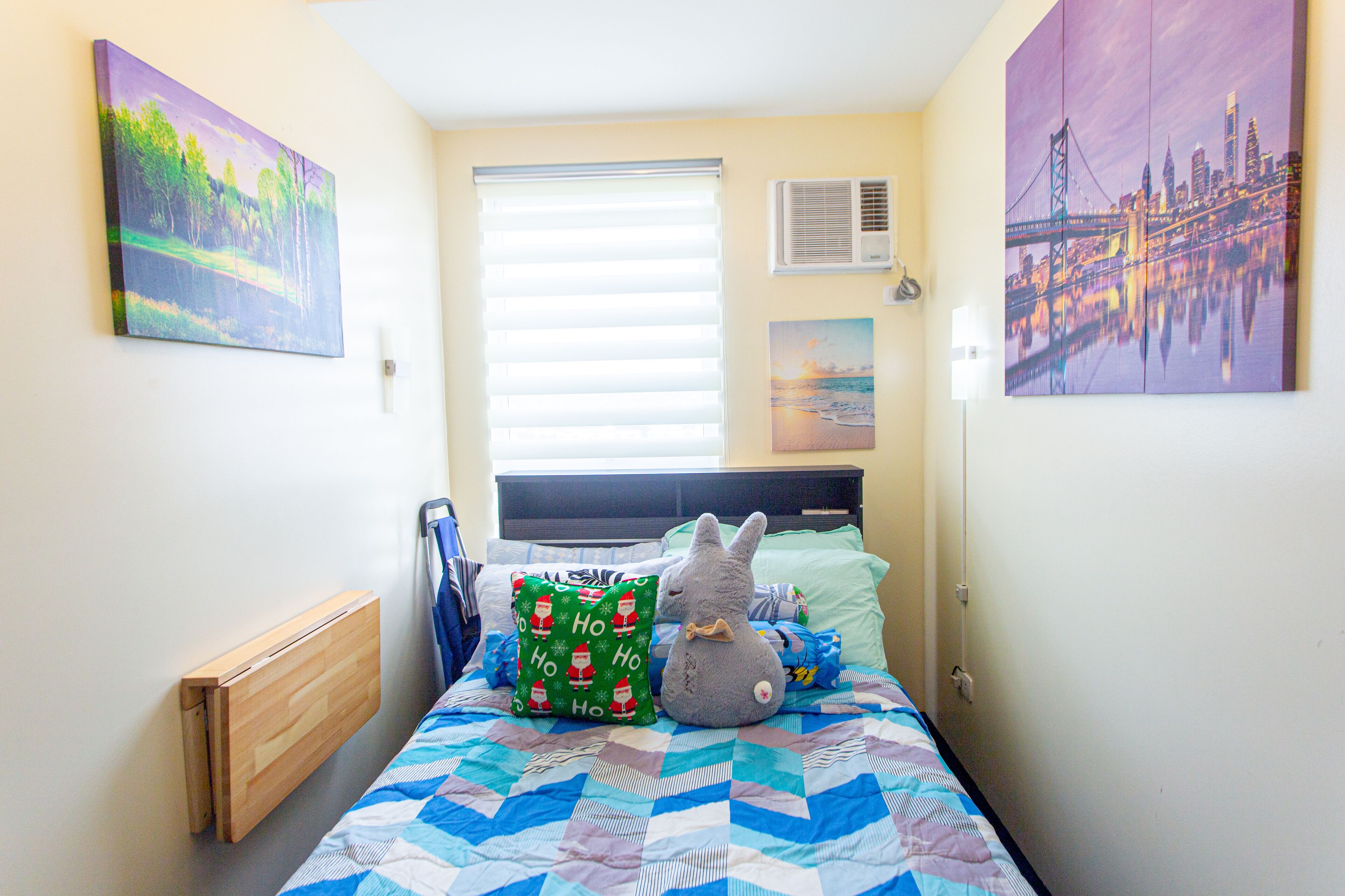 A bedroom with a bed, a radiator, a window with blinds, and two wall-mounted air conditioners.