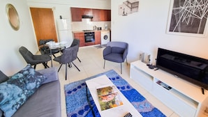 A modern living room with a sofa, a coffee table, a TV, and a dining area with chairs and a table. - Seaside Heaven Apartment (Larnaca)
