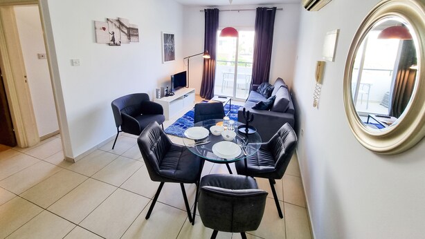 A modern living room with a dining area, featuring a sofa, chairs, a TV, and a dining table. - Seaside Heaven Apartment (Larnaca)