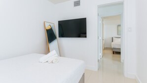 A modern hotel room with a bed, a flat-screen TV mounted on the wall, and a door leading to another room. - TC-1804 · Lovely 2BR in the Heart of Brickell, Free Parking (Miami)