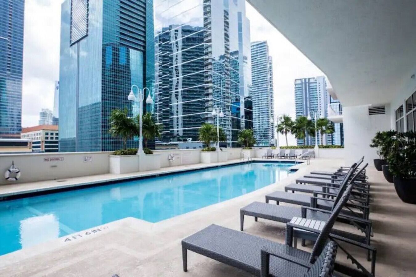 Una piscina en la azotea con sillones de descanso, rodeada de edificios altos.