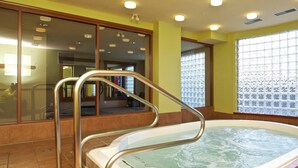Zona de spa con bañera de hidromasaje, pared de cristal y ventana con diseño decorativo.