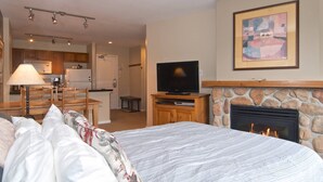 Un dormitorio con cama, televisión, chimenea y una cocina al fondo.