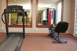 Ein Fitnessraum mit Laufband, Ergometer und einem Spiegel, der den Raum wiedergibt.