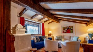 Een gezellige woonkamer met een open haard, houten balken, een zithoek en een kleurrijk vloerkleed.