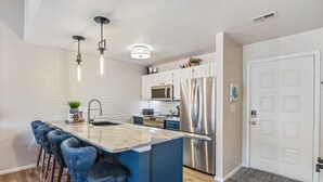 A modern kitchen with a central island, bar stools, stainless steel appliances, and pendant lighting.