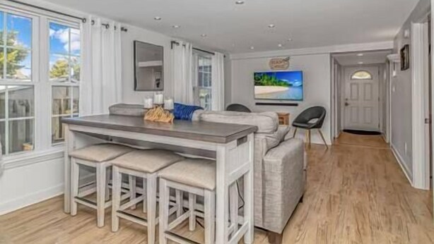 A modern kitchen with a central island, a dining area with a bench, and a TV mounted on the wall. - 7BR Family Oasis | Heated Pool + Walk to Beach (North Myrtle Beach)