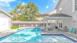 A backyard with a swimming pool, a covered patio area, and a fenced yard. - 7BR Family Oasis | Heated Pool + Walk to Beach (North Myrtle Beach)