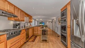 A kitchen with wooden cabinets, stainless steel appliances, and a central island. - 7BR Family Oasis | Heated Pool + Walk to Beach (North Myrtle Beach)