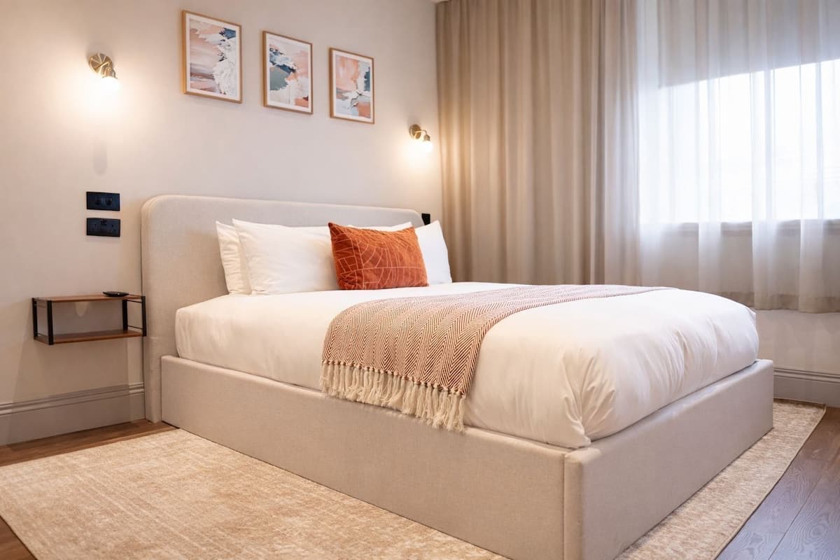 A modern bedroom with a large bed, a bedside table, and a wall-mounted light fixture.