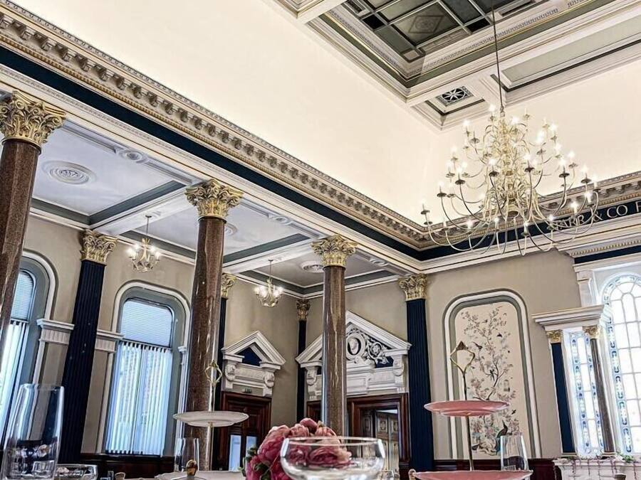 Un comedor amplio y lujoso con techo ornamentado y candelabros, ventanas grandes y una elegante vajilla.