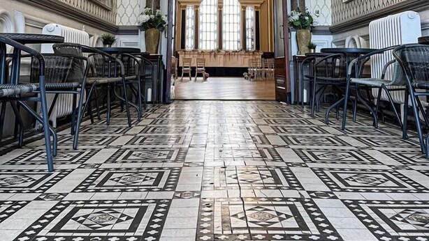 A grand hallway with patterned walls, a chandelier, and a view into a dining area with tables and chairs. - The Parrs Bank Hotel  (Warrington)