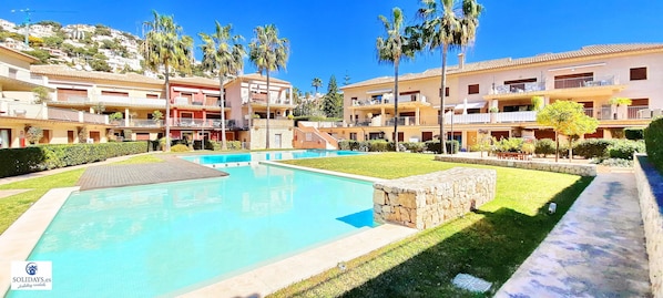 A resort with a swimming pool, multiple balconies, and palm trees.